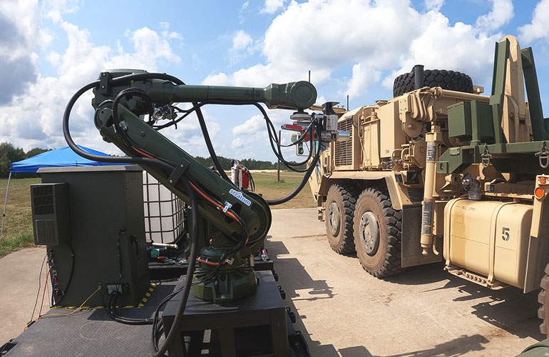 a robot arm hold a refueling hose next to a military vehicle