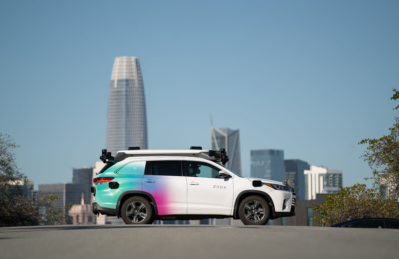 A white Toyota Highlander with blue and purple ombre in the back against a city skyline. 