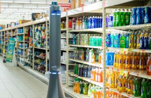 A tall, skinny pole-like robot moving down a grocery aisle with colorful products.