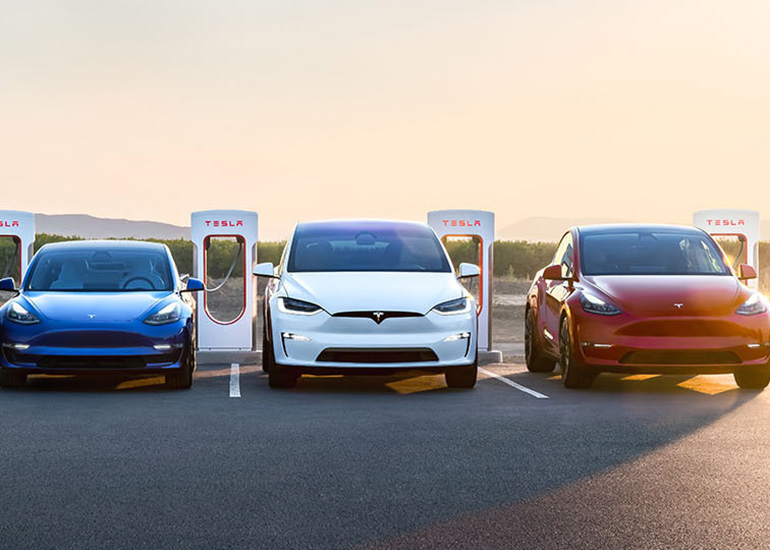 A blue, a white and a red Tesla car next to Tesla superchargers. 