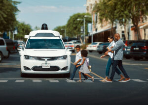 A Waymo car stopped at a crosswalk with a family walking in front of it.