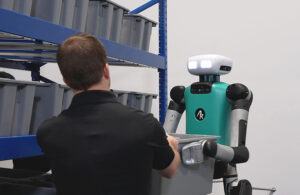 Agility Digit robot handing off a tote to a person in a black shirt.