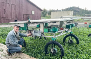 daniel theobald kneels next to his ag robotics platform on the farm.