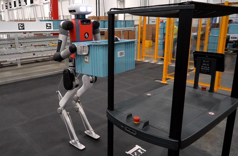 a digit humanoid robot lifting a tote off a mobile robot inside a SPANX warehouse.