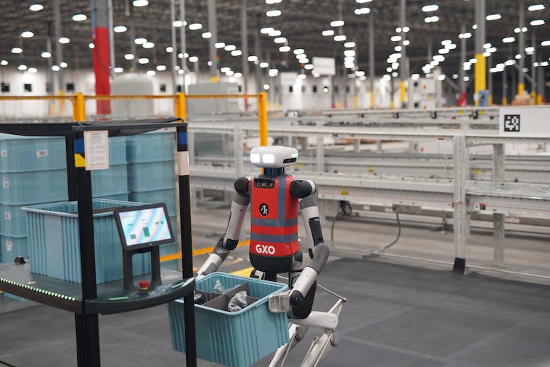 A Digit humanoid bending down to take a tote off the bottom shelf of a mobile robot.