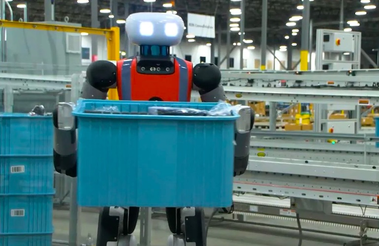 A Digit humanoid from Agility Robotics carrying a tote inside of a warehouse.