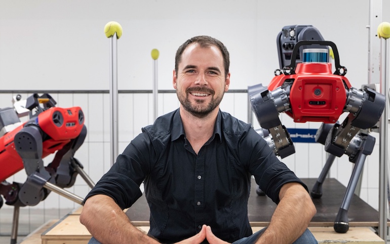 Dr. Marco Hutter sitting in front of two ANYmal quadruped robots.