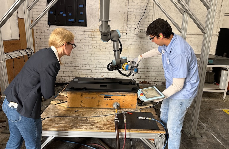 A worker programming a UR10e cobot arm to trim thermoformed plastic parts