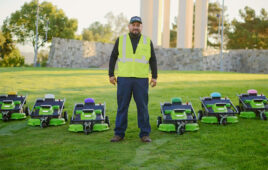 field workers stands on lawn surrounded by a fleet of autonomous electric sheep mowers.