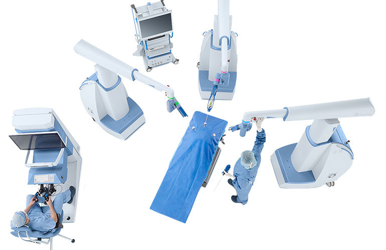 The Asensus Surgical Senhance Surgical System features three long robotic arms hovering over an empty hospital bed and a control station.