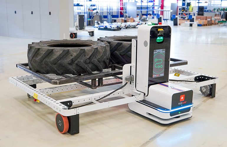 a Flexqube navigator AMR moves a rack with large tractor tires.