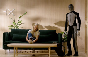 a young female ties her shoes on a couch next to a 1X NEO beta robot.