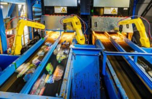 An image showing three yellow robotic arms picking items on a conveyor belt.