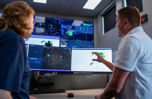 Two people facing away from the camera looking at two computer monitors.