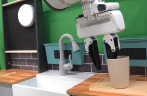 A robot arm with a two-fingered gripper picking up a cup next to a sink.