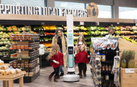 A woman with three daughters excitedly approaching a Tally robot in a grocery store.
