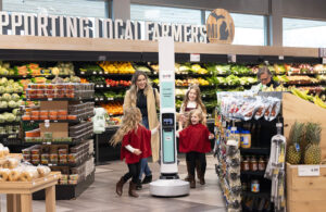 A woman with three daughters excitedly approaching a Tally robot in a grocery store.