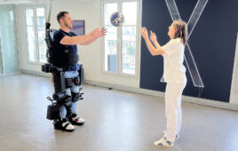 A person wearing a Wandercraft exoskeleton catching a ball thrown to them by a woman in white.