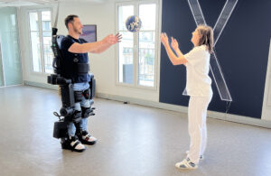 A person wearing a Wandercraft exoskeleton catching a ball thrown to them by a woman in white.