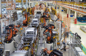 An automotive assembly line with several orange industrial robots building cars.