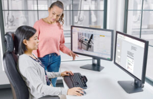 Two women looking at two monitors with ABB's robot studio on the screen.