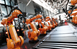 Orange robotic arms working on a manufacturing line.
