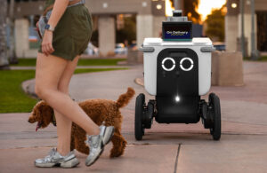 Sirva o robô de entrega Robotics com uma mulher e um cachorro passando.