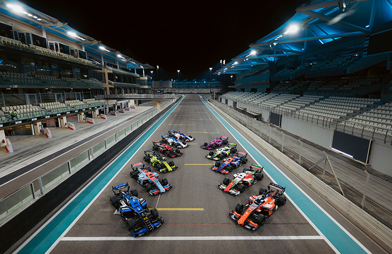 A2RL raceteam car lined up on the starting grid. There area 8 race cars, each with a unique and colorful livery.