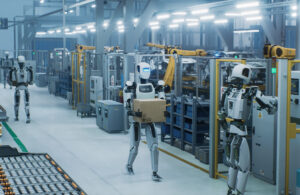 A humanoid robot carrying a box in an automated facility.