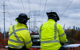 Two people looking at a computer and watching a drone string powerlines.