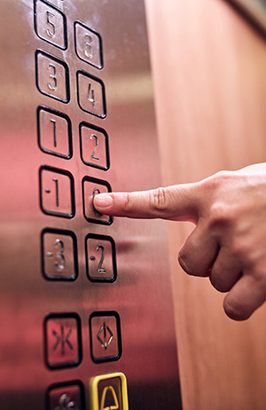 a hand pushing an elevator button. Otis has integrated its elevators with mobile robots.