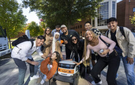 Students on a college campus smiling with a delivery robot from Starship Technologies.