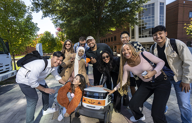 Students on a college campus smiling with a delivery robot from Starship Technologies.