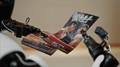 AGIBOT WORLD 2026 trains on real-world scenarios, such as this bimanual manipulation of flyers.