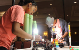 two kids working with robots on a table top field.