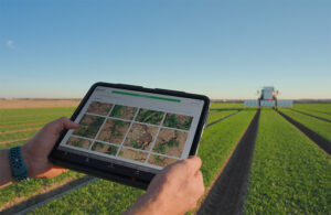 close up of an ipad in foreground with a tractor in a field in the background.