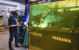 A robot arm welding behind a protective barrier.