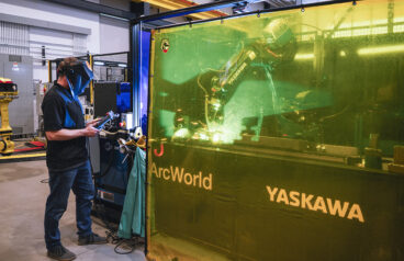 A robot arm welding behind a protective barrier.