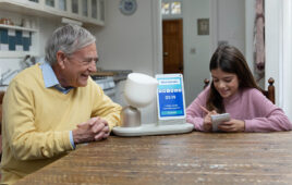 A man and young girl playing a game using the ElliQ robot.
