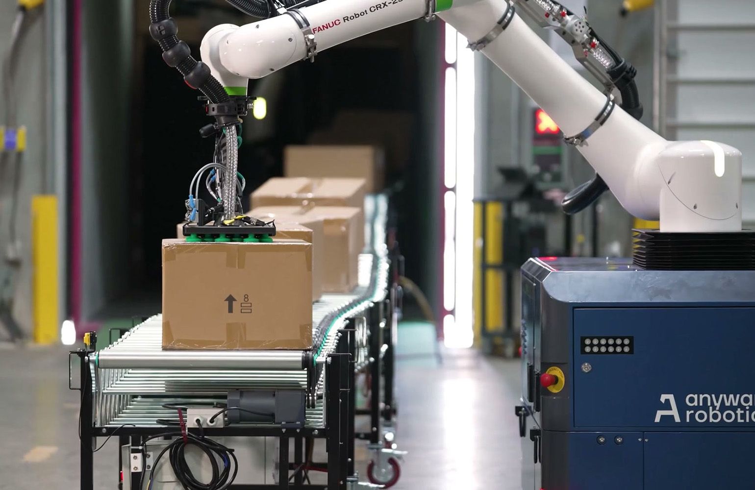 A robot arm picking a box from a conveyor belt.