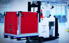 A Dematic automated forklift picking up a large red box.