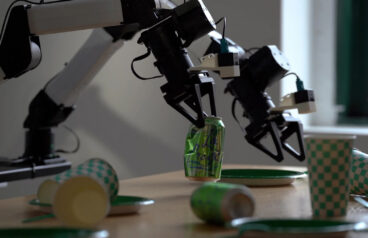 Two robot arms cleaning a table. One holds an empty can.
